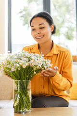 Smiling beautiful African American woman florist holding daisies bouquet sitting in floral shop. Small business owner concept 