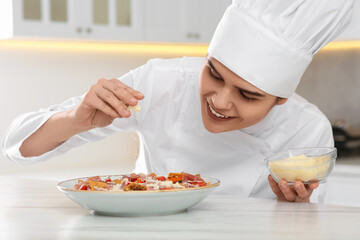 Professional chef adding grated cheese into delicious dish in kitchen
