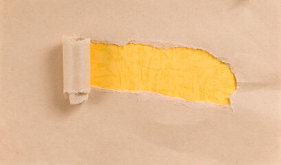 A torn piece of kraft paper revealing yellow paper underneath