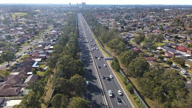 Aerial drone pullback reverse view above the South Western M5 Motorway at Casula in Sydney, NSW Australia with Liverpool CBD in the background 