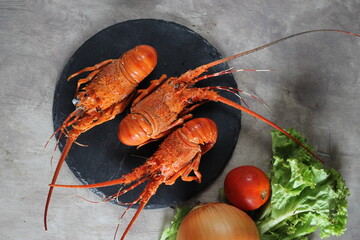 Three perfectly cooked lobsters on black slate with onion, lettuce and tomato in the background. Selective focus