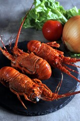 Three perfectly cooked lobsters on black slate with onion, lettuce and tomato in the background. Selective focus