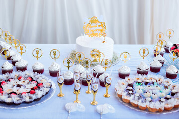 a tray of colorful sweets, a white cake with gold and cupcakes on a table with a white tablecloth