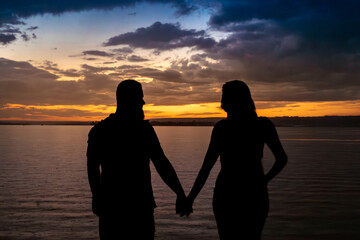 the silhouette of a couple beside a lake in the late afternoon with a blue and yellow gradient sky