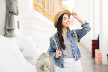 Portrait of Asian female traveler walking on walkway of the temple while smiling back in Bangkok, Thailand, Southeast Asia - Woman enjoying solo backpacking lifestyle - with copy space - 616860588