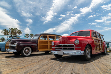 Beautiful woody classic cars on display during a hot summer afternoon under a cloudy sky.