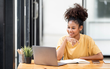 Joyful black woman in yellow shirt smiling toothily and using laptop for online learning at home.