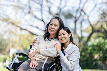 Fototapeta na wymiar Asian senior woman in wheelchair with happy daughter. Family relationship retired woman sitting on wheelchair in the park age care at retirement home.