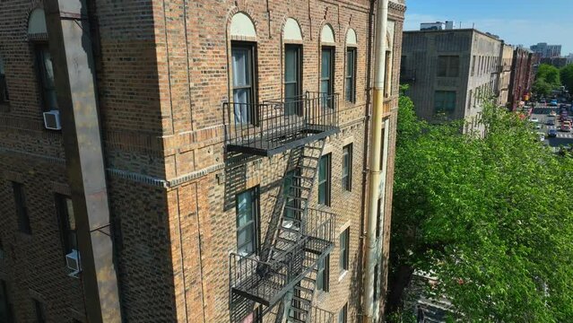 Aerial descending shot of old apartment complex in New York City with fire escape and window air conditioning units in summer.