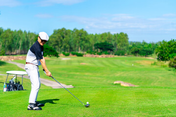 Confidence Asian man golfer holding golf club hitting golf ball on golf course fairway in sunny day. Healthy people enjoy outdoor activity  lifestyle sport golfing at country club on summer vacation.