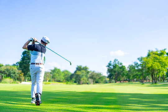 Confidence Asian man golfer holding golf club hitting golf ball on golf course fairway in sunny day. Healthy people enjoy outdoor activity  lifestyle sport golfing at country club on summer vacation.