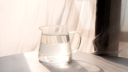 Glass cup of drinking water with reflection of sunlight on the table. minimalistic concept