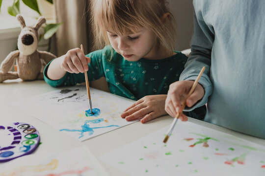 Two cute little sisters, classmates are painting on table. Small girl kids with brush in school. Happy adorable preschooler, 4 and 7 years child in living room. Home schooling concept, doing homework