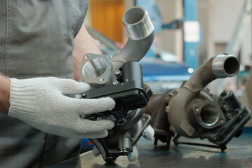 Car service. An auto mechanic replaces a faulty turbocharger. The mechanic has a new turbocharger...