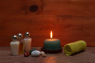 Obraz na płótnie Canvas Bath elements: shampoo, cream, green towel, stones and aromatic candle on a wooden background
