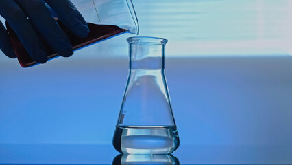 Chemical experiment. Pharmaceutical testing. Technician hand in rubber protective glove pouring red solution into glass tube with transparent liquid.