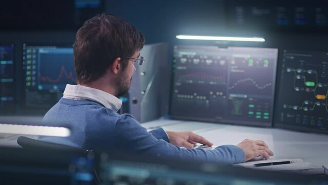 Professional software engineer sits in front of computer with big data server and blockchain network, works in modern monitoring control room with real-time analysis charts. Concept of cyber security.
