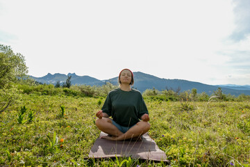 Naklejka na ściany i meble Wman doing yoga on blossom meadow and mountains background. Morning healthy activity.