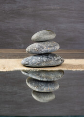 zen stones piled up on sand reflected in a mirror
