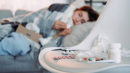 Home medicines. Healing pills. Variety of tablets flu treatment sick girl on blur laying on couch...