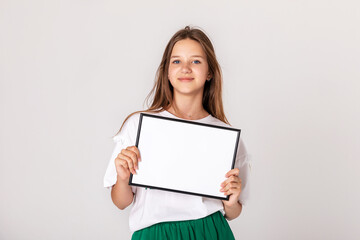 Naklejka premium White banner .Teenager girl hold white blank paper. Young smiling woman show blank board. Close up female model portrait on white background.