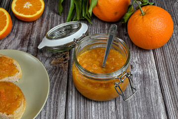Delicious homemade orange marmalade in an open glass jar with teaspoon inside. Homemade dessert on a wooden table. Top view, white background.