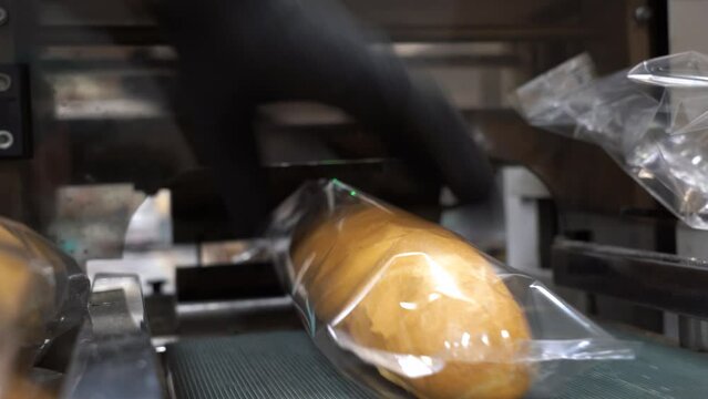 Fresh Bread Being Wrapped in Clear Packaging Film at Bread Packaging Line. Production Line Worker Works at the Bread Factory. Loaves of Bread Wrapped in Transparent Packaging.