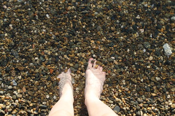 Bare feet in the water by the sea, person standing in the water by the sea shore, clear water