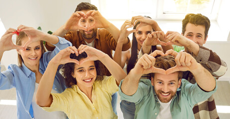 Group of happy, joyful, beautiful young people standing together, looking up, smiling and forming hearts with their hands. Top view high angle shot from above. Banner background. Love, support concept - obrazy, fototapety, plakaty