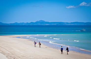 Two couples walk on an ideal beach on Keppel Island, Queensland, Australia. Sun-soaked sand beside...