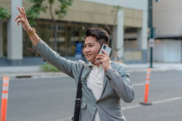 A young male employee on the go tries to hail a taxi while talking to a client over the phone. A busy and hectic work lifestyle.