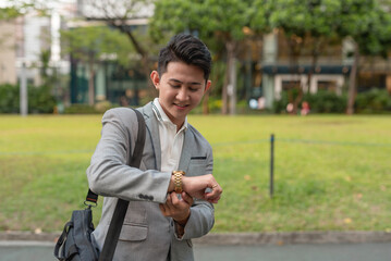 A young male employee on the go checks his watch for the time. Walking to work.