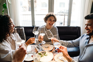 Group of smiling friends clinking wine glasses while dining in restaurant