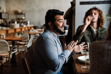 Cheerful indian man talking with friends while dining in restaurant