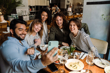 Group of joyful friends taking selfie while dining in restaurant