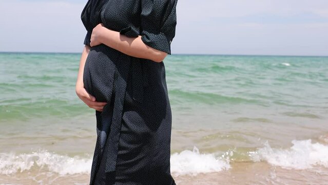 임산부가 그녀의 배를 안고 해변을 걷는다