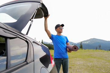 Men standing near car with open trunk planning to do yoga on mat. Outdoor yoga in mountains