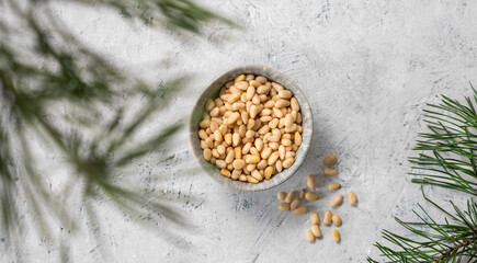 Pine nuts in a bowl  and a scattered on a light background with branches of pine needles. The concept of a natural, organic and healthy superfood and snack.
