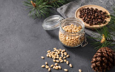 Pine nuts in a jar, bowl and a scattered on a dark background with branches of pine needles and cone. The concept of a natural, organic and healthy superfood and snack.