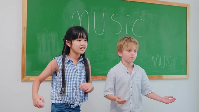 Adorable cute pupil show dancing in music subject front of classroom  at kindergarten school. Happy students making fun activity in school at elementary school.