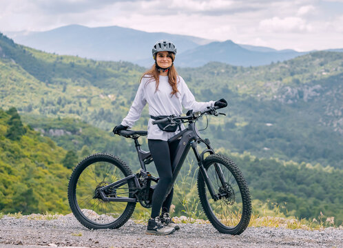 Happy girl wearing helmet and sportswear with her hightech electric bicycle on top of a canyon