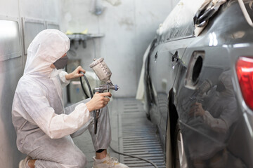 Worker painting a car in a special garage, wearing a white costume at car service 