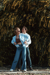 Obraz premium Outdoor shot of young couple in love walking on pathway through field. Man and woman walking along yellow flowering trees. 