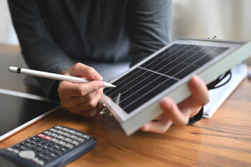 Alternative energy engineers hold solar panels samples while learning design and calculation for energy accumulation in photovoltaic panels installed with a calculator in the office.