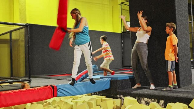 Smiling positive girls in sportswear having funny wrestling by inflatable logs in indoor game trampoline club