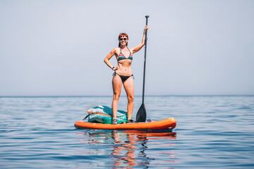 Happy gorgeous girl with a paddle swims on a sup board on the sea. Healthy lifestyle and recreation...