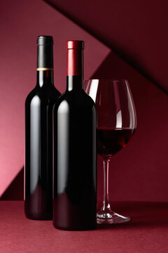 Glass and bottles of red wine on a red background.