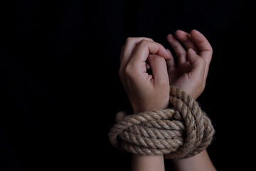 woman's hands tied with rope on black background, concept of domestic violence of the victim