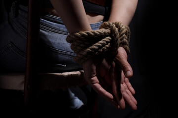 woman sits on a chair with her hands tied with a rope, the concept of violence, women's rights - obrazy, fototapety, plakaty