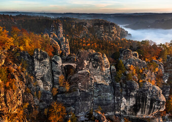 Saxon, Germany - Aerial view of the Bastei Bridge on a foggy autumn morning with colorful autumn foliage and heavy fog under the rock. Bastei is a rock formation in Saxon Switzerland National Park